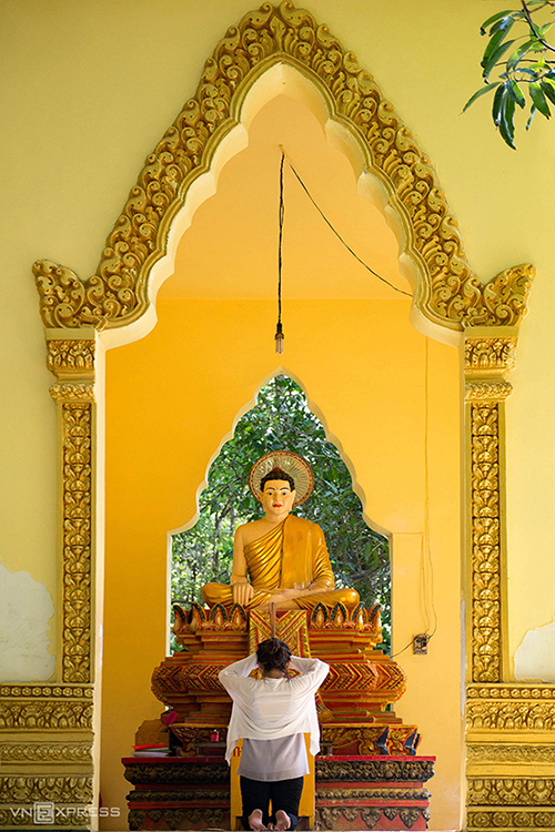 In the pagoda’s courtyard, a woman kneels and offers incense to the 1.5-meter high Gautama Buddha statue made of monolithic stone with a pedestal decorated with typical Khmer motifs.