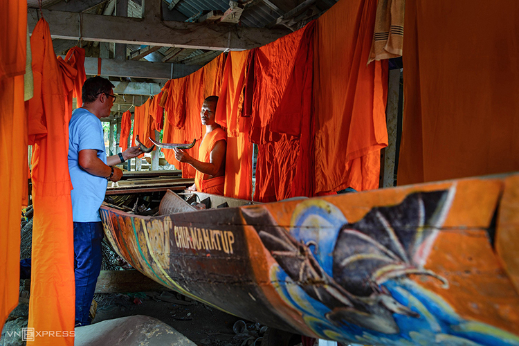 A monk shows a guest a small boat model next to a life-sized one.