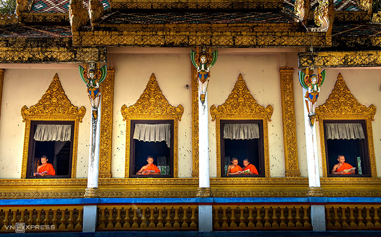 Novice monks read by the pagoda's windows. Next to them are columns with embossed statues of Khmer maidens praying.