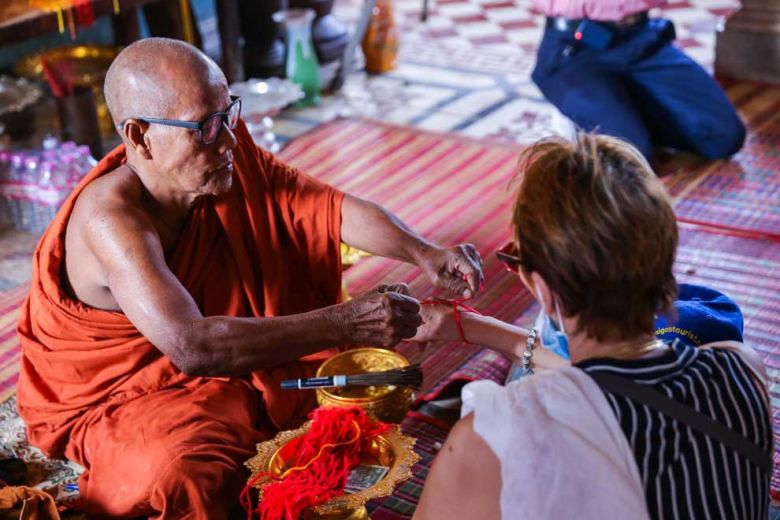 The pagoda’s chief monk, Men Tot, ties bracelets made out of red thread around a tourist’s wrist for luck.